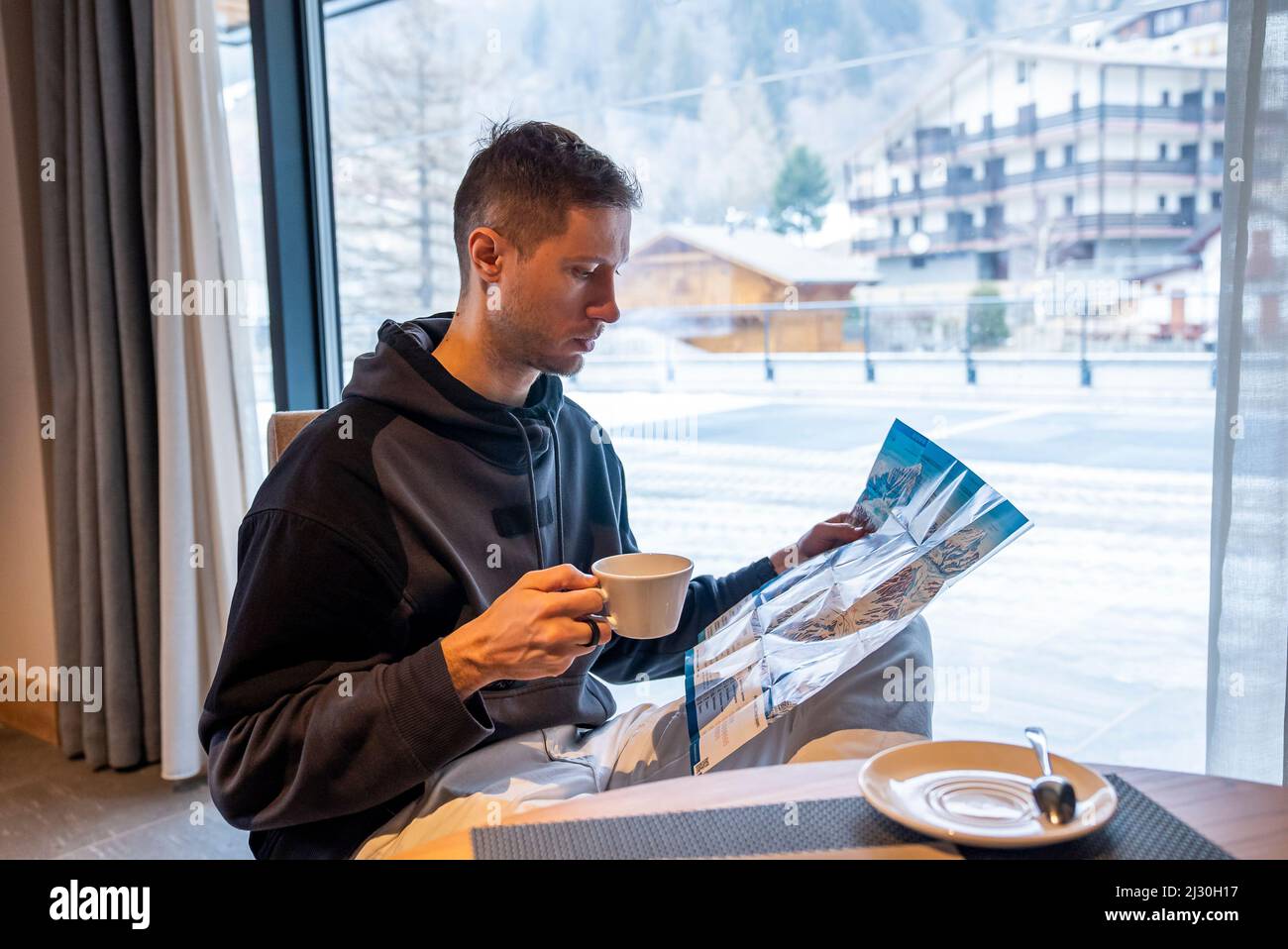 Männlicher Tourist, der die Skikarte analysiert, während er Kaffee im Resort Cafe trinkt Stockfoto