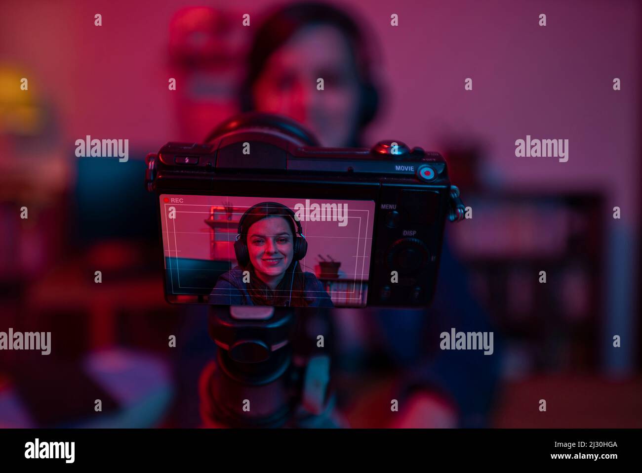 Nahaufnahme eines Kamerabildschirms, der eine wunderschöne hispanische Frau vor einer Videokamera aufzeichnet, die einen Blog in ihrem Studio mit roten und blauen Lichtern aufzeichnet Stockfoto