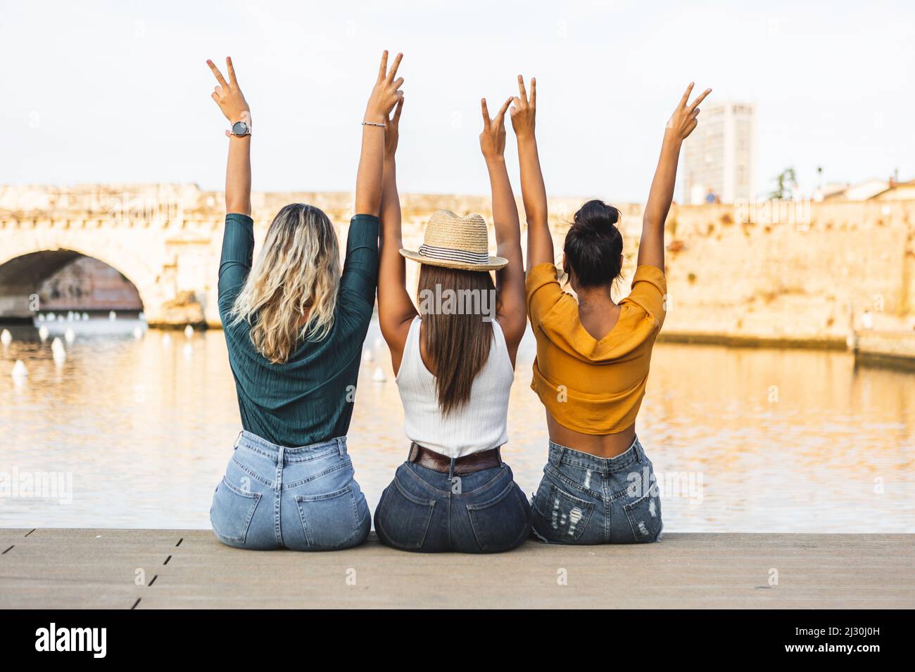 Rückansicht von drei multirassischen Freundinnen mit erhobenen Händen im Freien Stockfoto