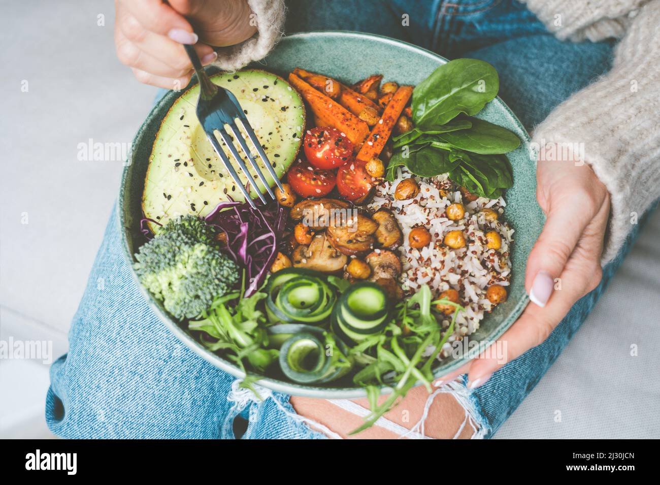 Frau, die eine gesunde Mahlzeit isst. Schüssel mit Reis, Quinoa, Avocado, Gurke, Brokkoli und Gurke. Gesunde Ernährung, Mittag- oder Abendessen. Gesunder Teller Stockfoto