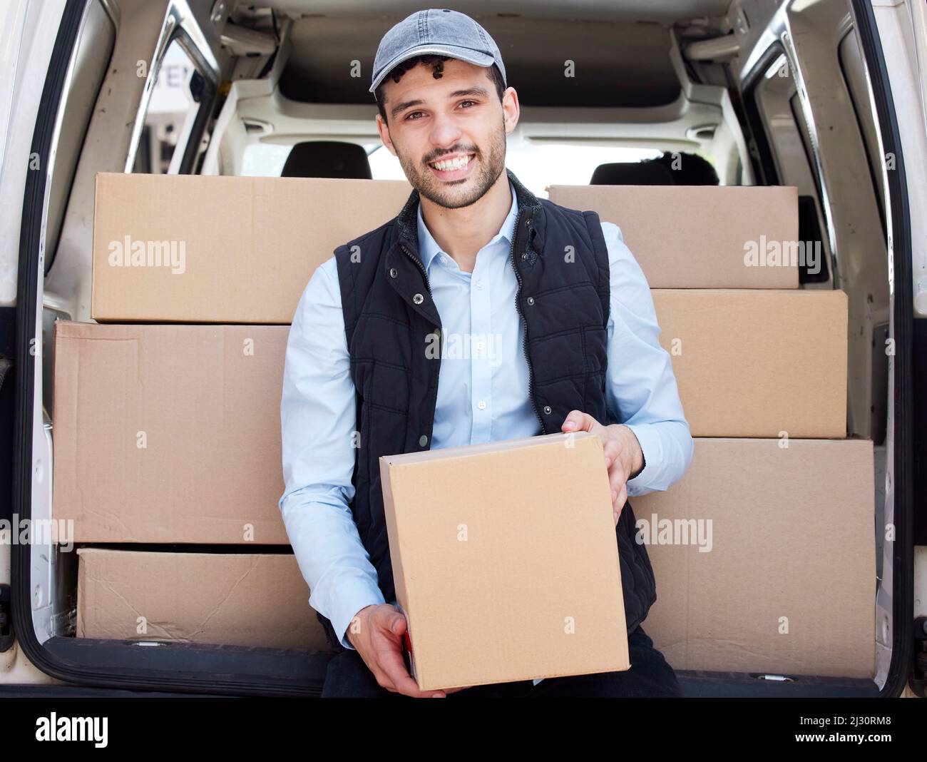 Auf dem Weg zum nächsten Karton. Porträt eines jungen Lieferers, der Kisten aus einem Lieferwagen lade. Stockfoto