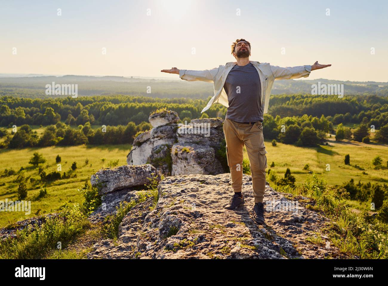 Junger Mann, der an sonnigen Tagen mit offenen Armen auf dem Berg steht, genießt eine Sommerwanderung Stockfoto