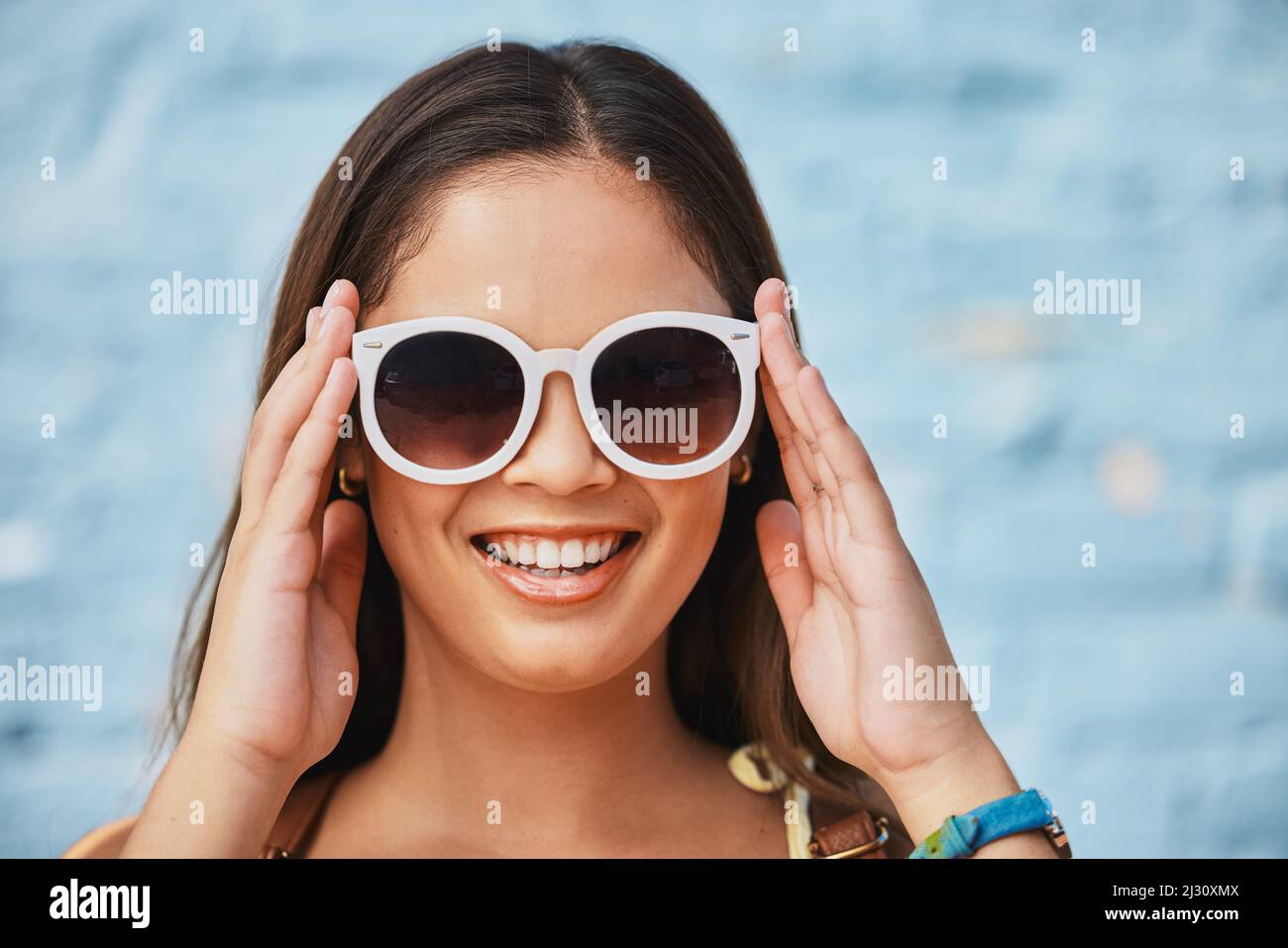 Shades on und bereit für den Sommer. Das verkürzte Porträt einer attraktiven jungen Frau, die ihre Sommertöne draußen vor einem blauen Hintergrund trägt. Stockfoto