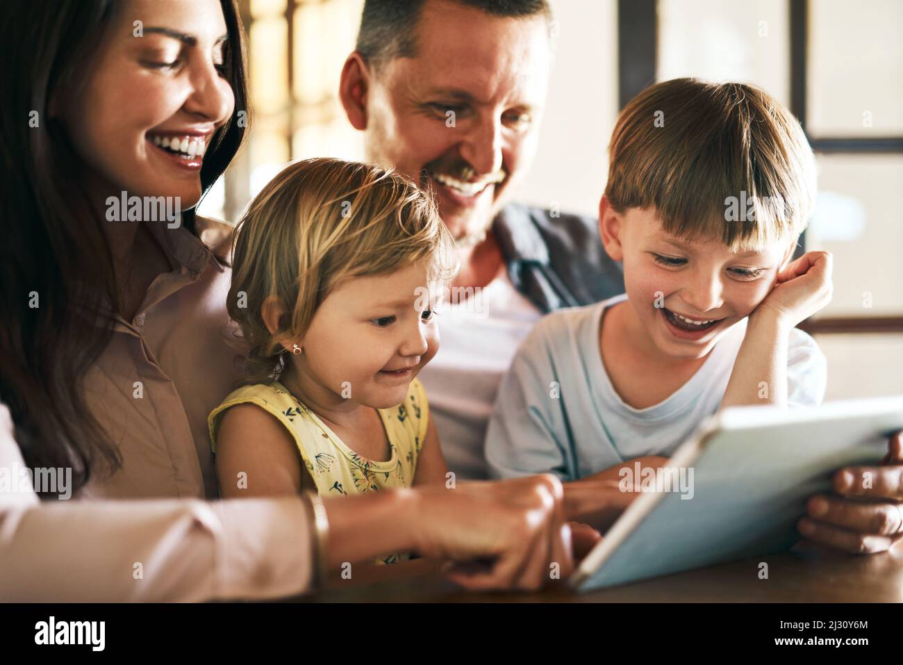 Hinzufügen von Bildschirmzeit zur Familienzeit. Aufnahme einer jungen vierköpfigen Familie, die zu Hause ein digitales Tablet verwendet. Stockfoto