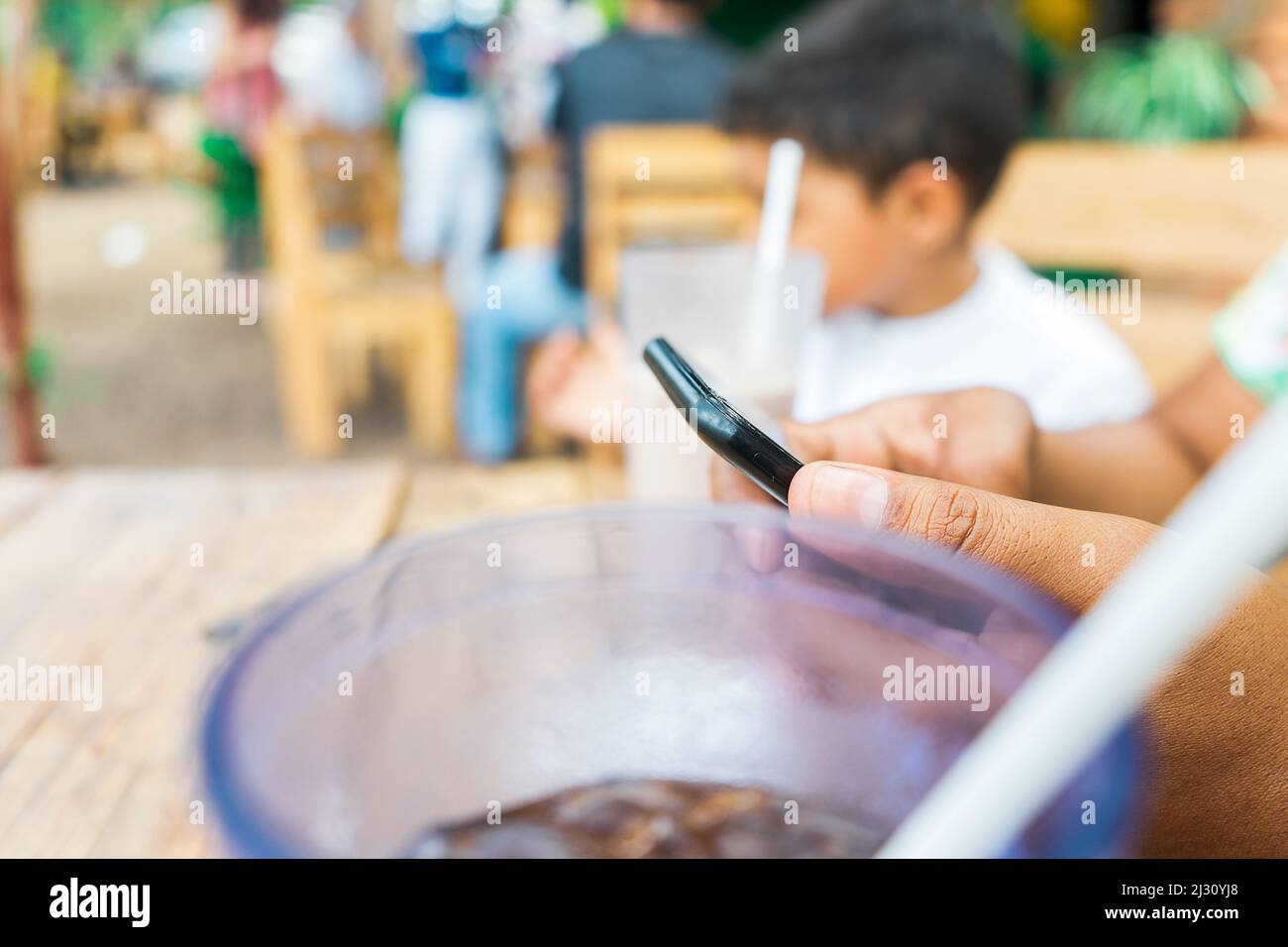 Nahaufnahme der Hände einer lateinischen Mutter abgelenkt auf ihrem Handy, während mit ihrem Sohn Stockfoto