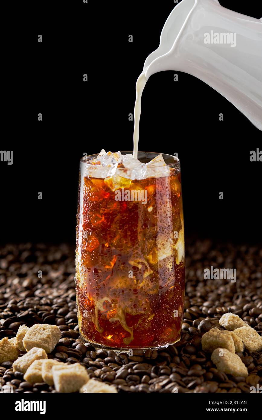 Eiskaffee. Leckerer Eiskaffee mit Milch, kaltes Getränk im Glas mit Eis auf dunklem Kaffeehintergrund. Stockfoto
