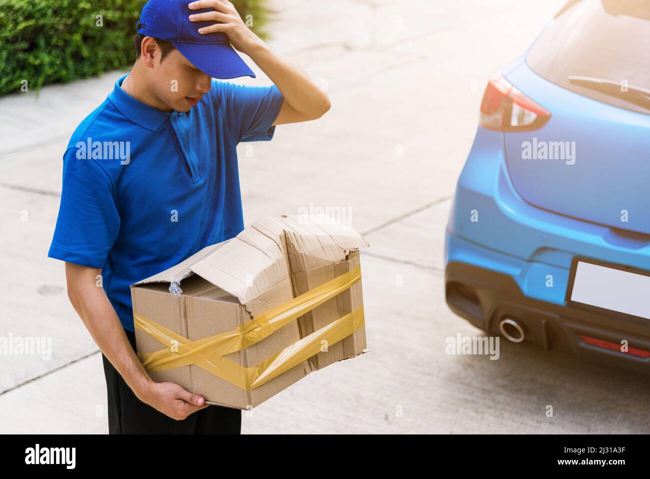 Asiatische junge Lieferung Mann in blauer Uniform er emotional fallen Kurier halten beschädigte Karton ist an der Tür vor Hause gebrochen, Unfall schlechten Transport Stockfoto