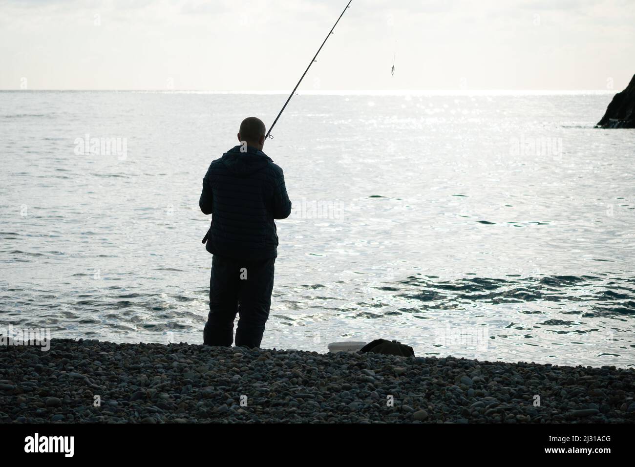 Mann Hobby Angeln auf dem Meer strafft eine Angelschnur Haspel von Fischen. Ruhiges Oberflächenmeer. Nahaufnahme einer Fischer-Hände-Drehspule mit Angelschnur auf einer Rute Stockfoto