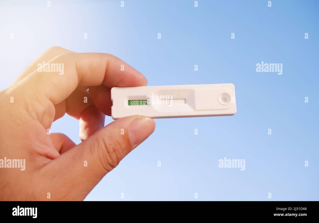 Eigene Hand mit negativem Covid-19-Testergebnis mit SARS CoV-2 Rapid Antigen Test Kit (ATK) und blauem Himmel-Hintergrund mit Sonnenlicht, Coronavirus-Infecti Stockfoto