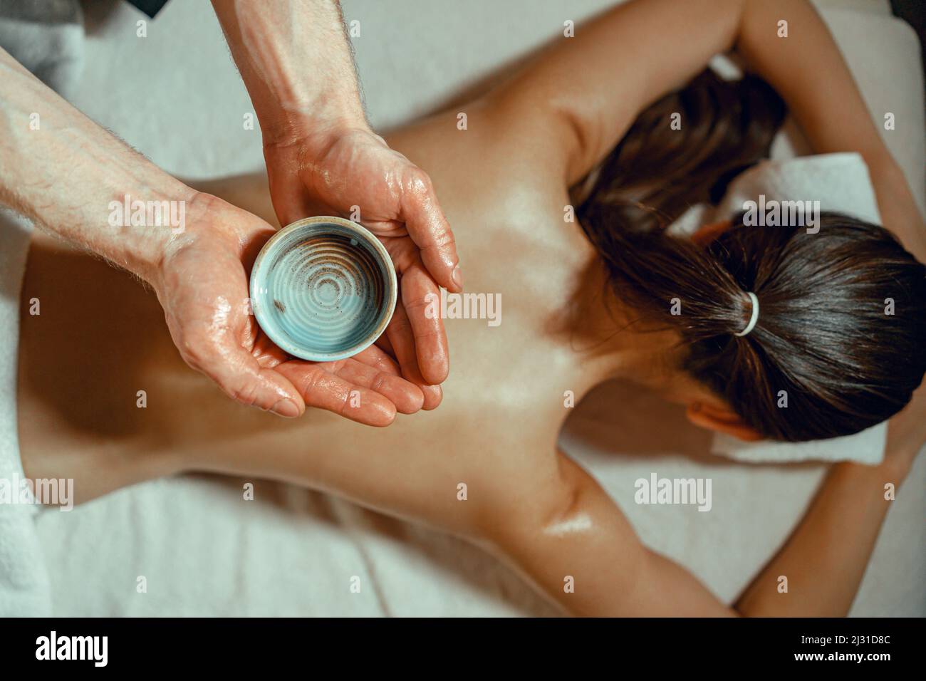 Masseur Mann hält Schüssel mit warmem Kraut infundiert Öl für Rückenmassage Stockfoto