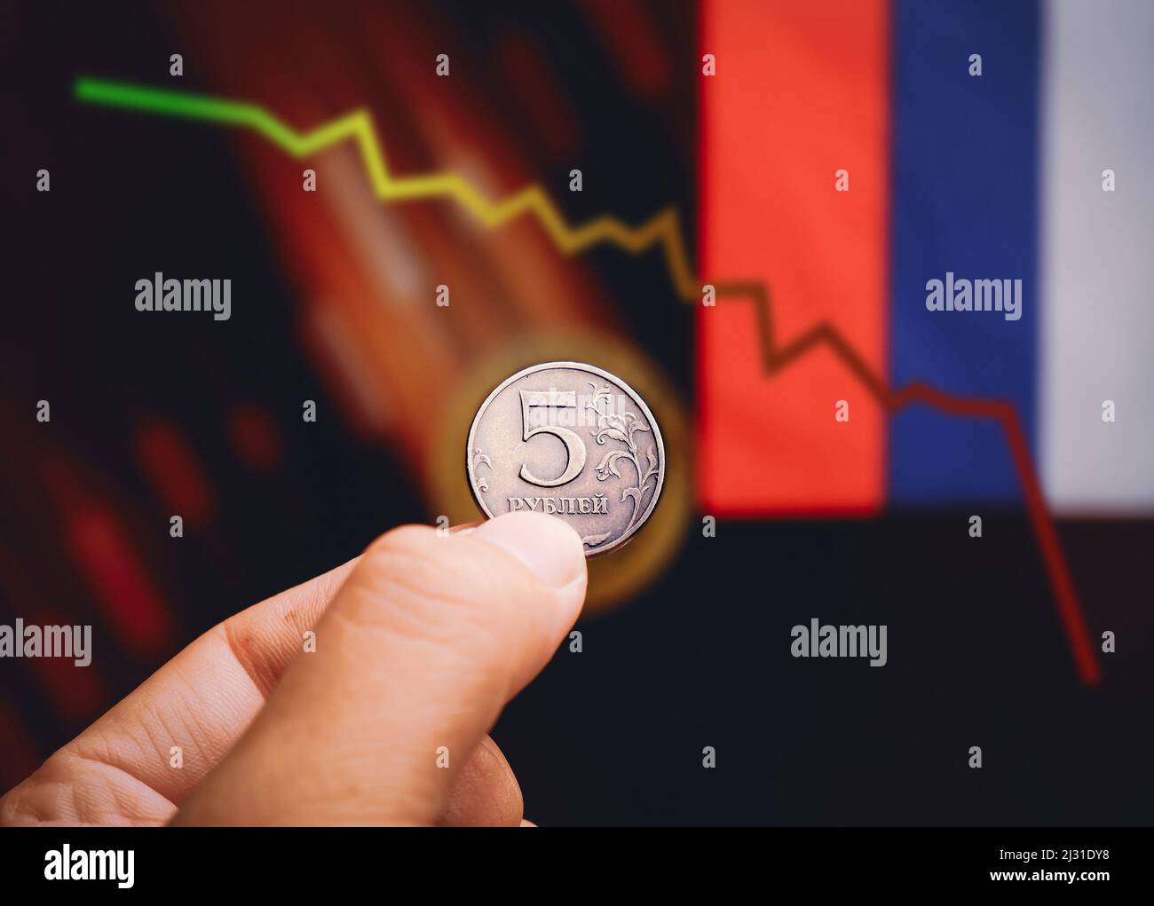 Russische Rubel-Münze hält auf der Hand mit fallenden Trading-Charts und russischen Flaggen verschwommen Hintergrund Stockfoto