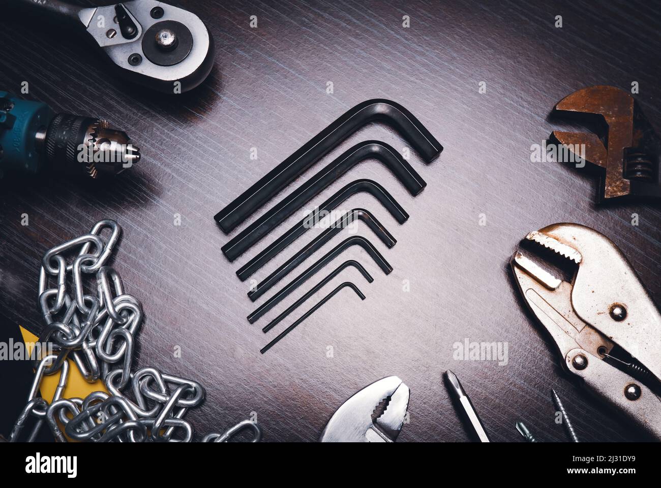 L-förmige Sechskantwerkzeuge auf dem Hartholztisch in der Mitte mit mechanischen Werkzeugen neben, Low-Key Stockfoto