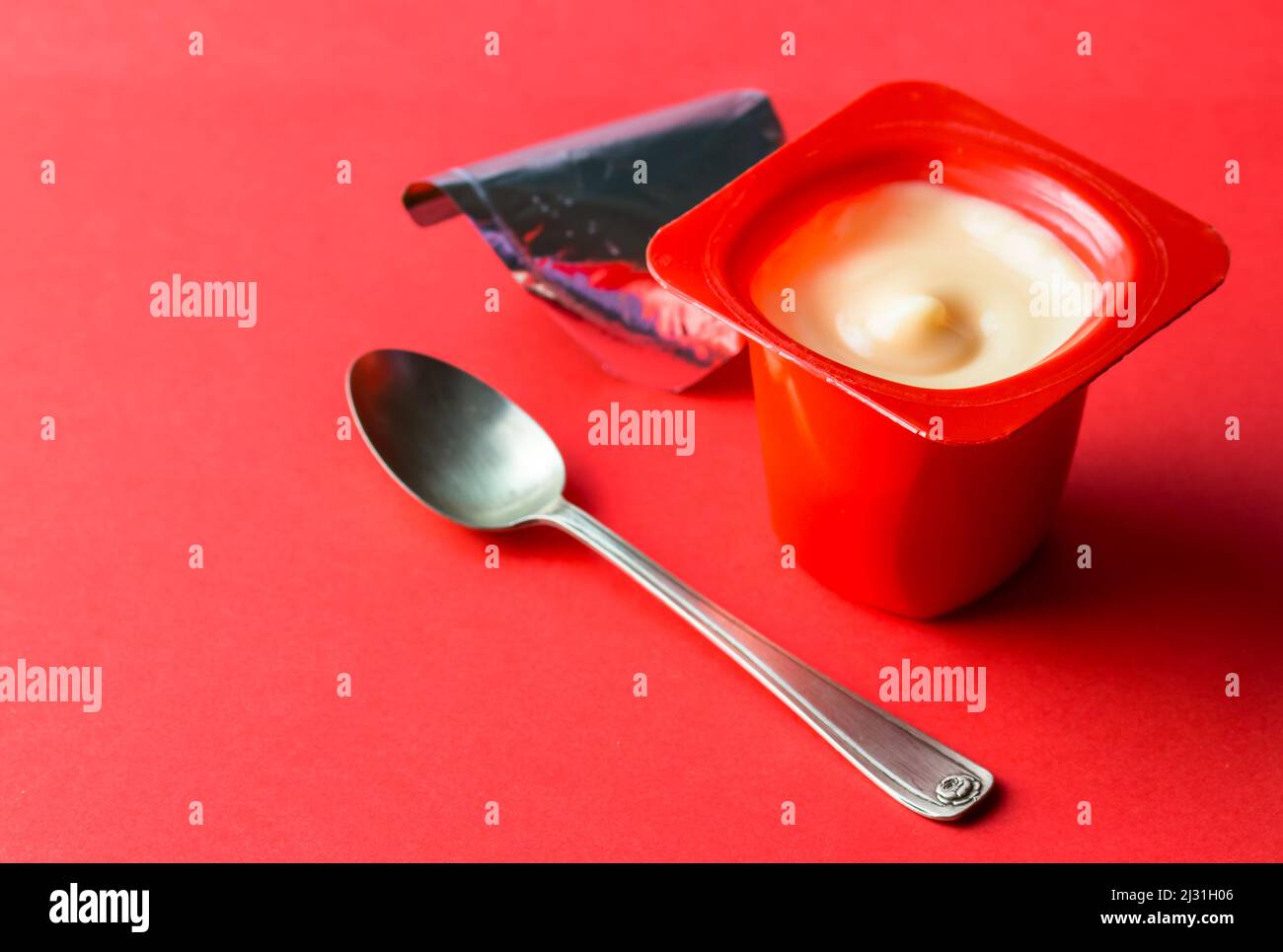 Cremig weißer, geöffneter Joghurt-Kunststofftopf. Isoliert auf rot mit selektivem Fokus und Kopierbereich Stockfoto