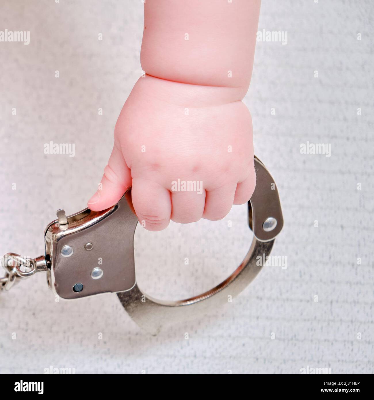 Babyhand und Handschellen, Nahaufnahme. Kinder Finger und ein Objekt auf weißem Hintergrund Stockfoto