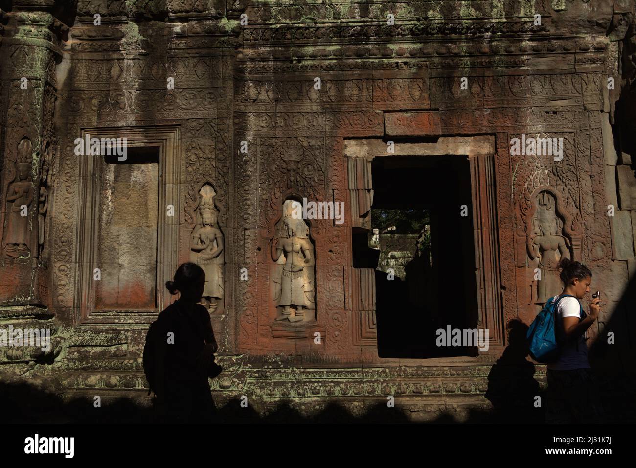 Frauen, die vor einer Mauer auf dem mit apsara-Figuren geschmückten Ta Prohm Tempelgelände in Siem Reap, Kambodscha, spazieren. Einst als Drehort für einen Hollywood-Film von 2001 verwendet Lara Croft: Tomb Raider mit Angelina Jolie und vor allem bekannt für seine riesigen Wurzeln aus wilden Bäumen, die tief zwischen den Steinen verwurzelt sind, war Ta Prohm ein Kloster für Studenten des Mahayana-Buddhismus, bevor es verlassen und für Hunderte von Jahren vergessen wurde. Stockfoto