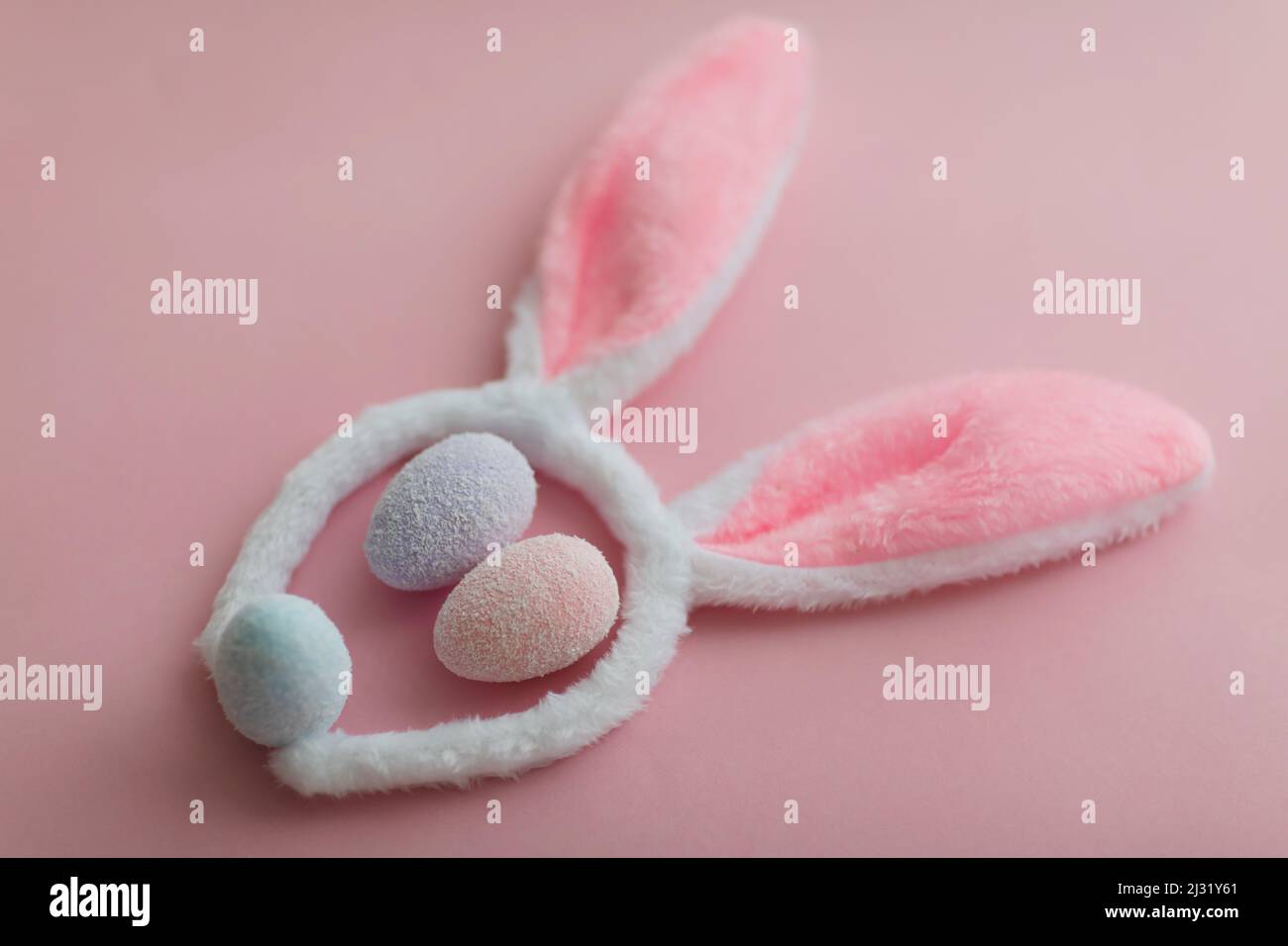 Hasengesicht aus Hasenohren und bunten Eiern auf rosa Hintergrund. Minimales Osterkonzept. Stockfoto