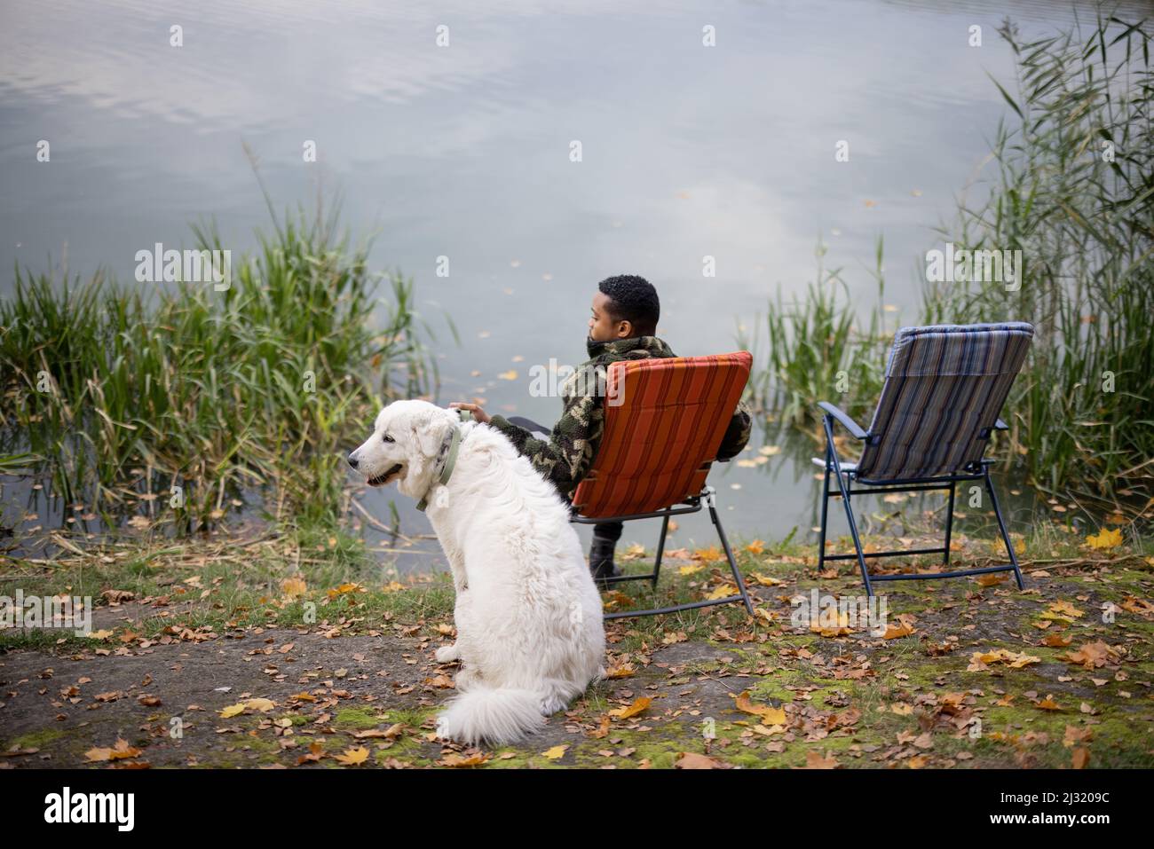Mann, der in der Nähe des Hundes an der Fluss- oder Seenküste angeln kann Stockfoto