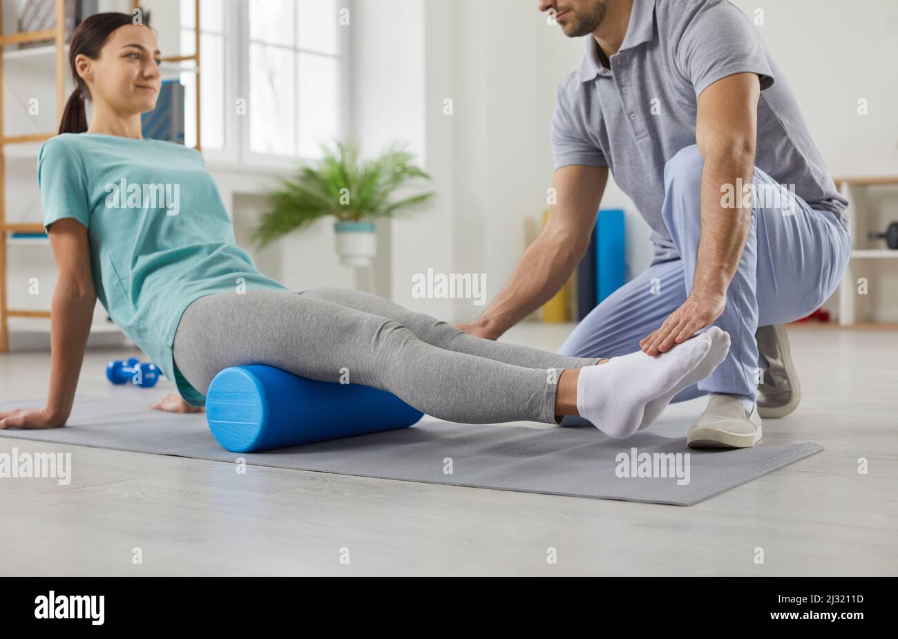 Physiotherapeutin schult junge Frau mit Schaumstoffwalze im modernen Rehabilitationszentrum. Stockfoto