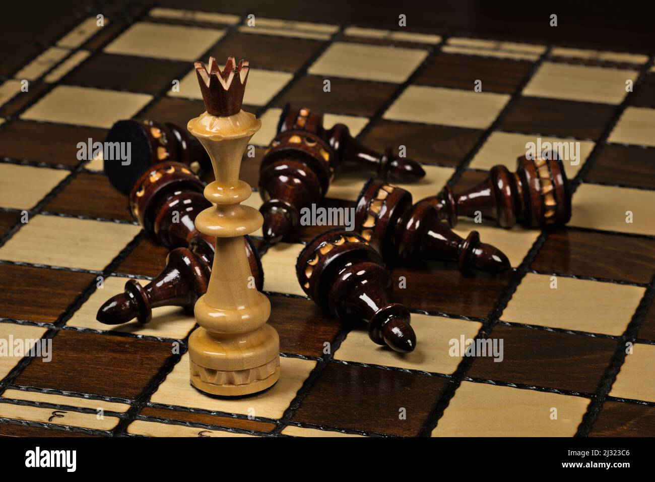 Weißer König, der auf einem Schachbrett vor liegenden schwarzen Bauern steht Stockfoto