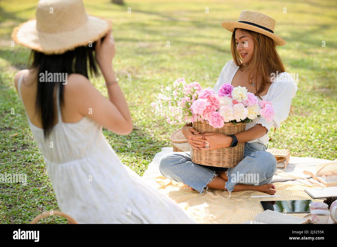 Zwei asiatische Frauen machen ein Picknick im grünen Park, haben eine schöne Zeit zusammen an einem schönen Sommertag, weibliche ein Foto für ihre Freundin. Stockfoto