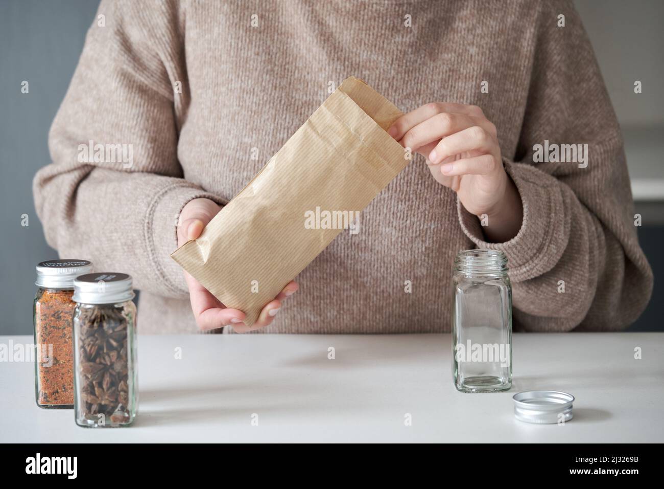 Nicht erkennbare Frau, die Gewürzglas aus einer Papiertüte nachfüllt. Stockfoto