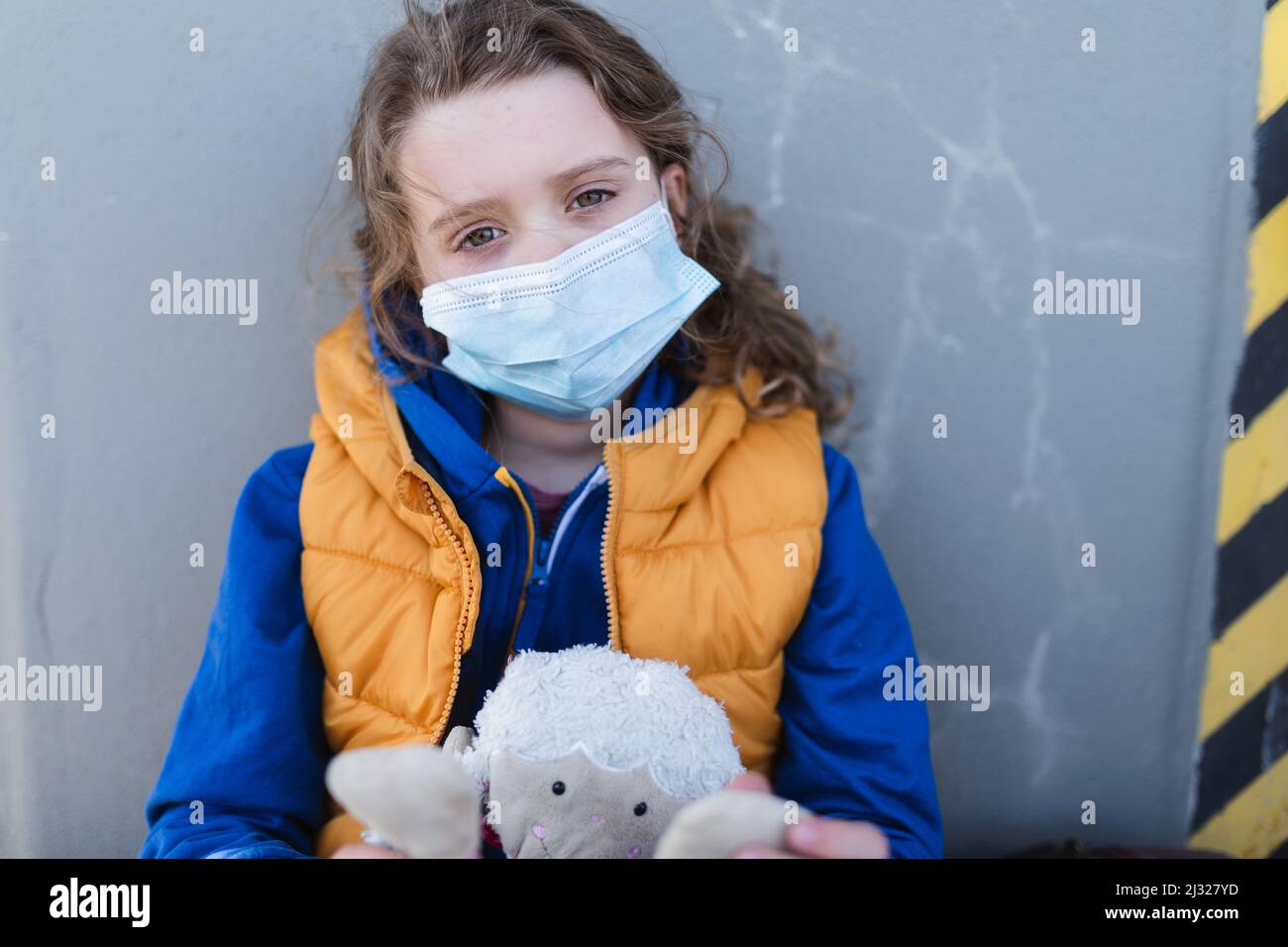 Trauriges ukrainisches Flüchtlingskind mit Gesichtsmaske wartet am Bahnhof, ukrainisches Kriegskonzept. Stockfoto