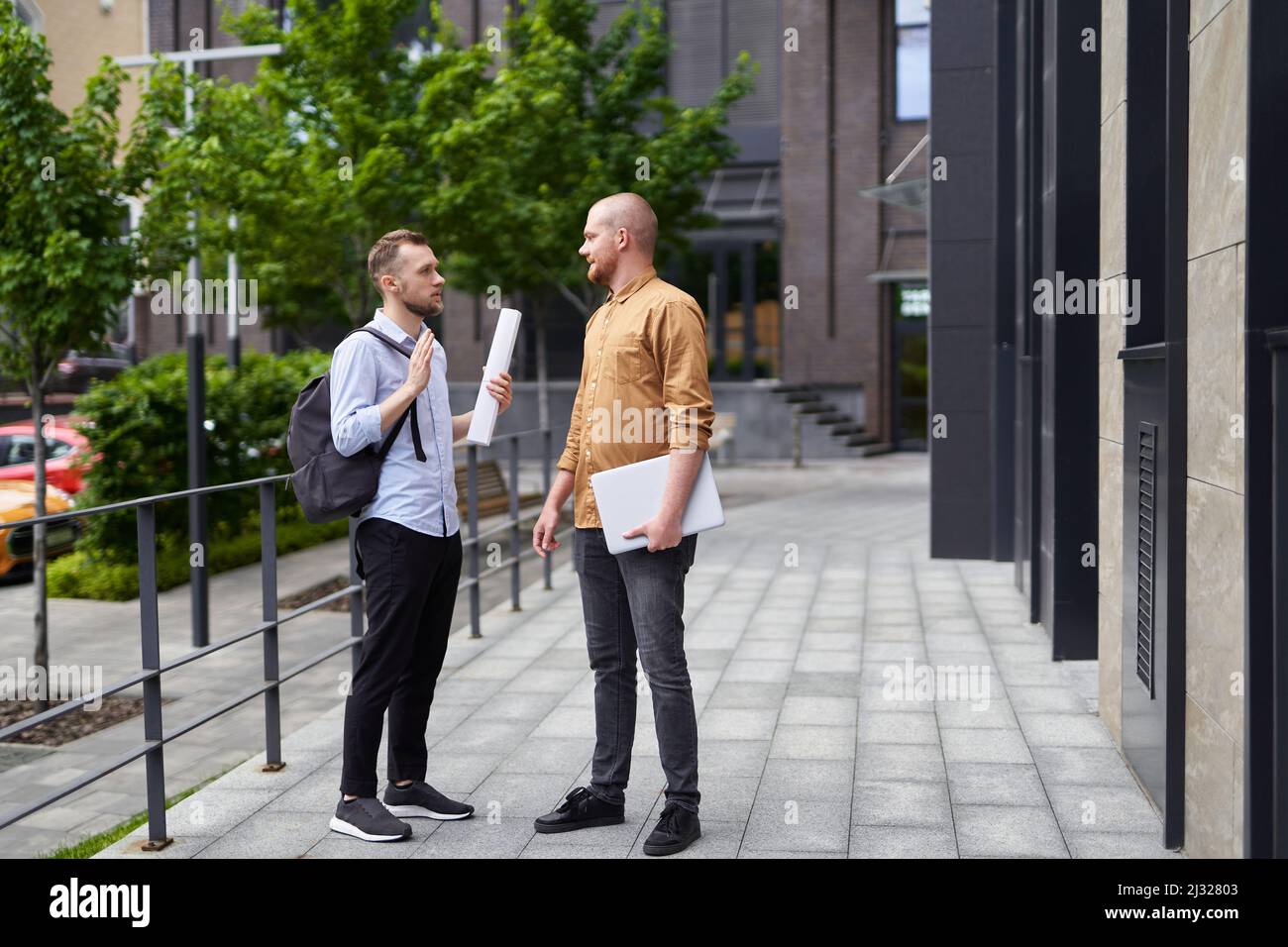 Männliche Immobilienmakler sprechen draußen mit Blaupausen und Laptop. Bau-, Architektur- oder Design-Manager Konzept. Unterwegs treffen in der Innenstadt. Hochwertige Bilder Stockfoto