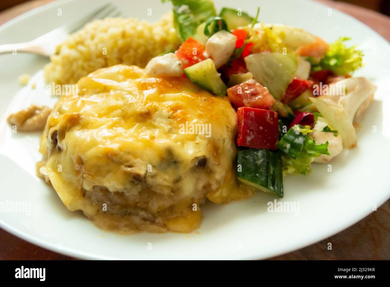 Abendessen Gericht mit großen gehackten Schnitzel mit gelbem Käse und Salat mit roten Paprika, Gurke und weißem Käse. Stockfoto