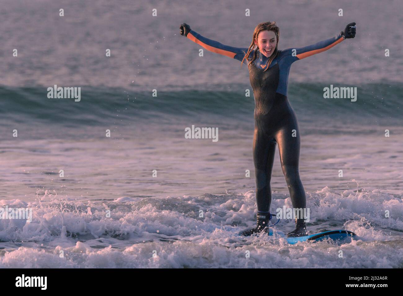 Eine junge Surferin feiert ihr erstes Mal, dass sie auf einem Surfbrett am Fistral Beach in Newquay in Cornwall in Großbritannien aufsteht. Stockfoto