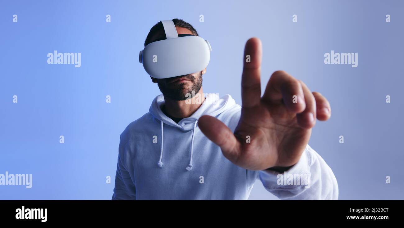 Mann berührt einen Knopf im virtuellen Raum. Junger Mann, der mit dem Metaverse über ein Virtual-Reality-Headset interagiert. Junger Mann, der 3D eine Simulation erlebt Stockfoto