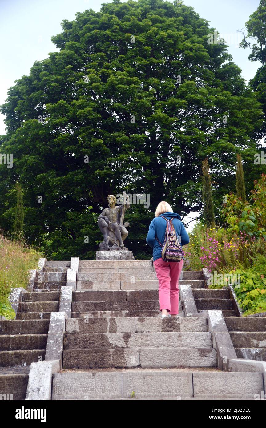 Frau, die die Stufen zur Neptune's Statue & Water Cascade in der Holker Hall & Gardens, Lake District, Cumbria, England, Großbritannien, hinaufgeht. Stockfoto
