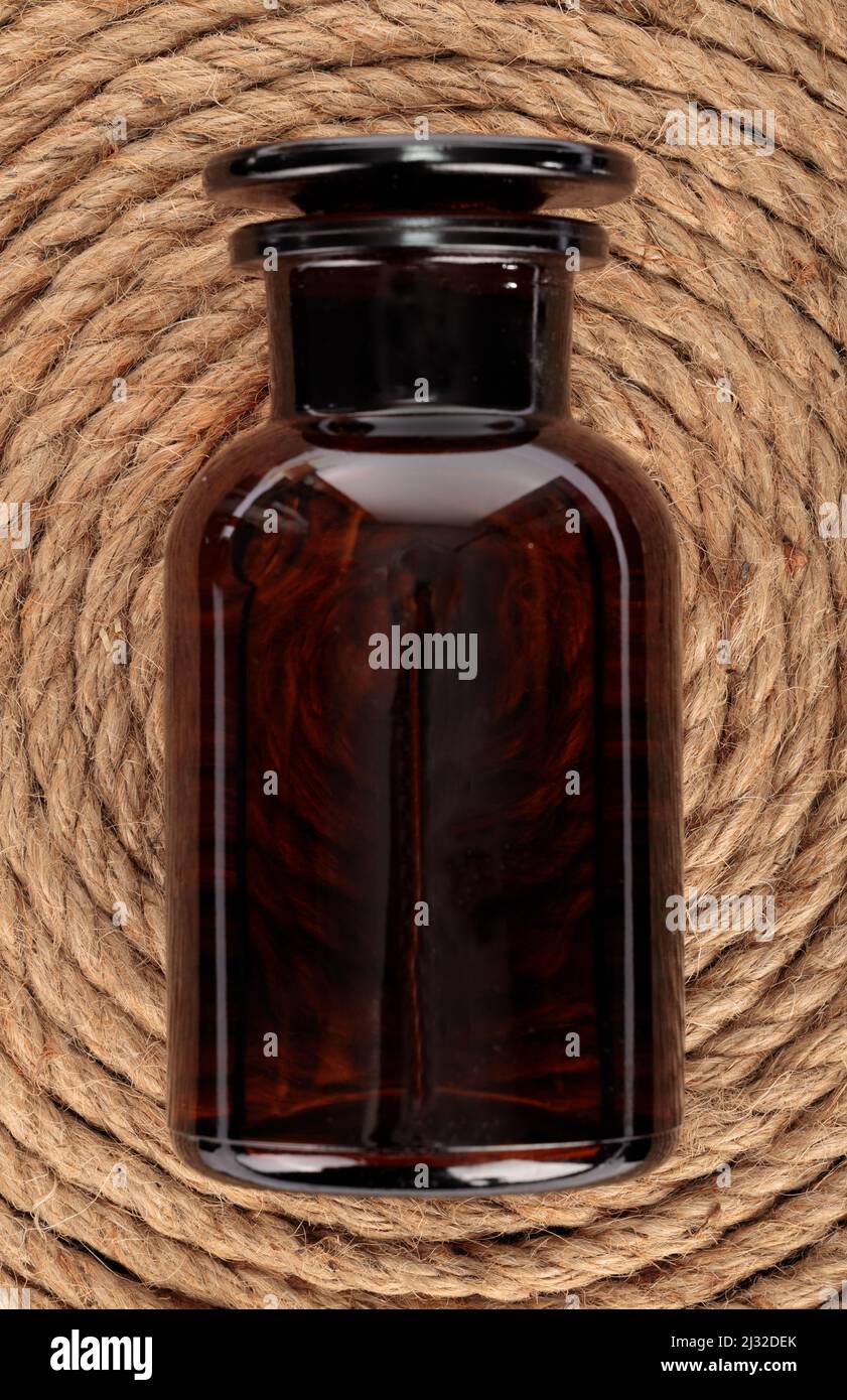 Eine vertikale Draufsicht auf eine leere medizinische braune Glasflasche auf einer runden Holzmatte Stockfoto