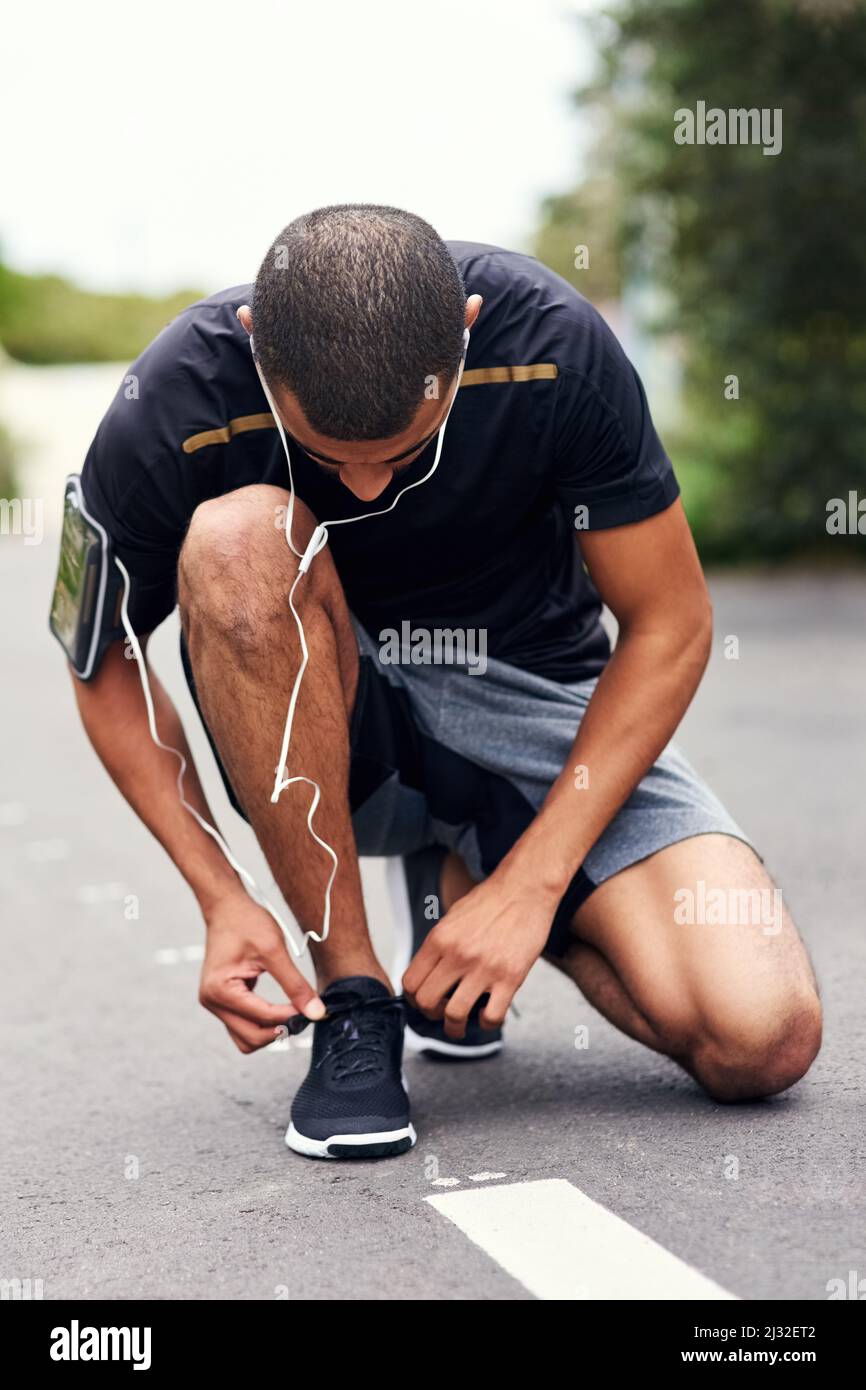 Immer bereit, sein Fitness-Spiel zu verstärken. Aufnahme eines sportlichen jungen Mannes, der seine Schnürsenkel beim Laufen bindet. Stockfoto
