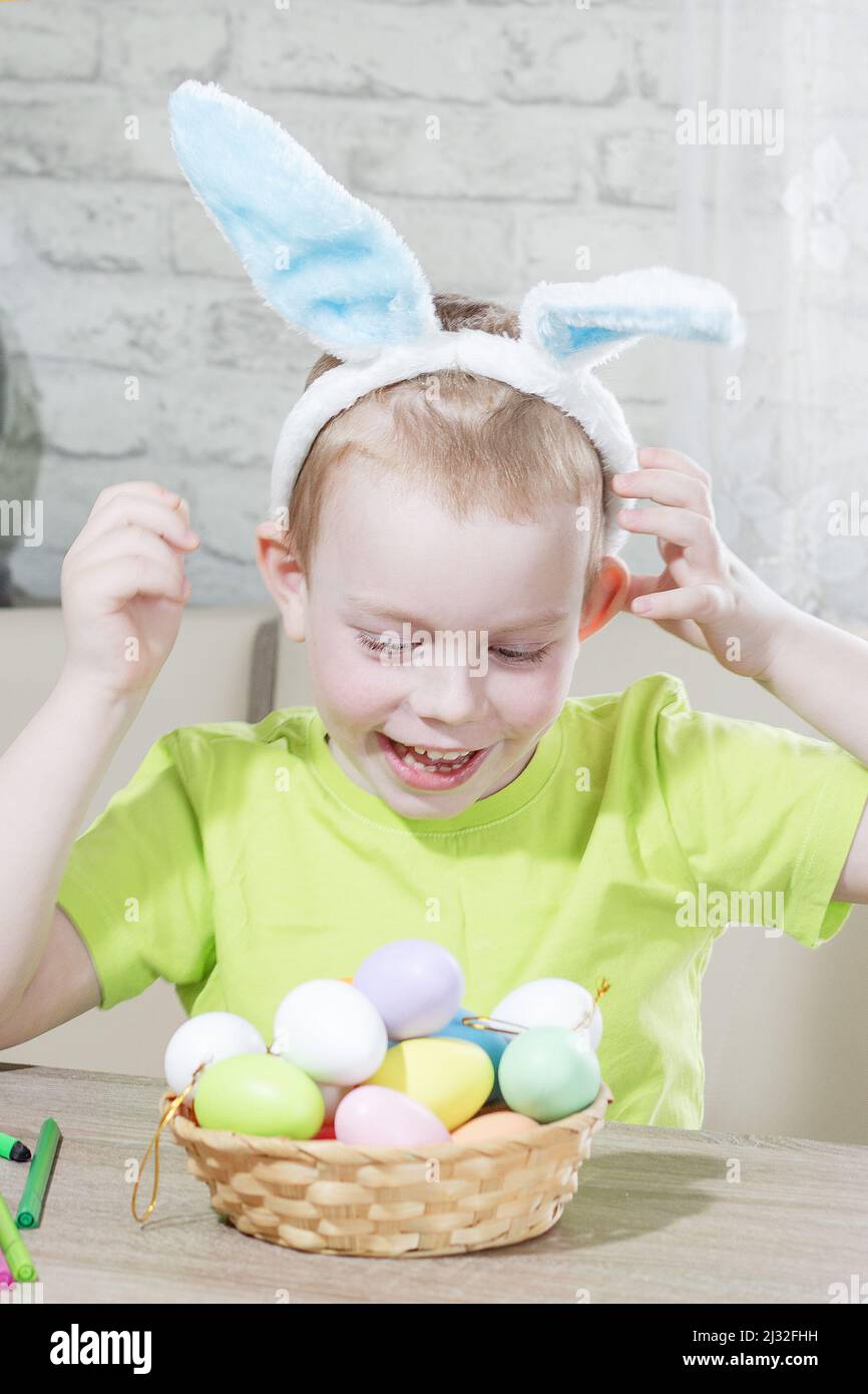 Osterkinder. Glücklicher Junge in Kaninchenohren auf dem Kopf spielt zu Hause mit bunten Eiern. Vorbereitung auf die Easter die große Eiersuche. Osterhase. Ostereier. Stockfoto