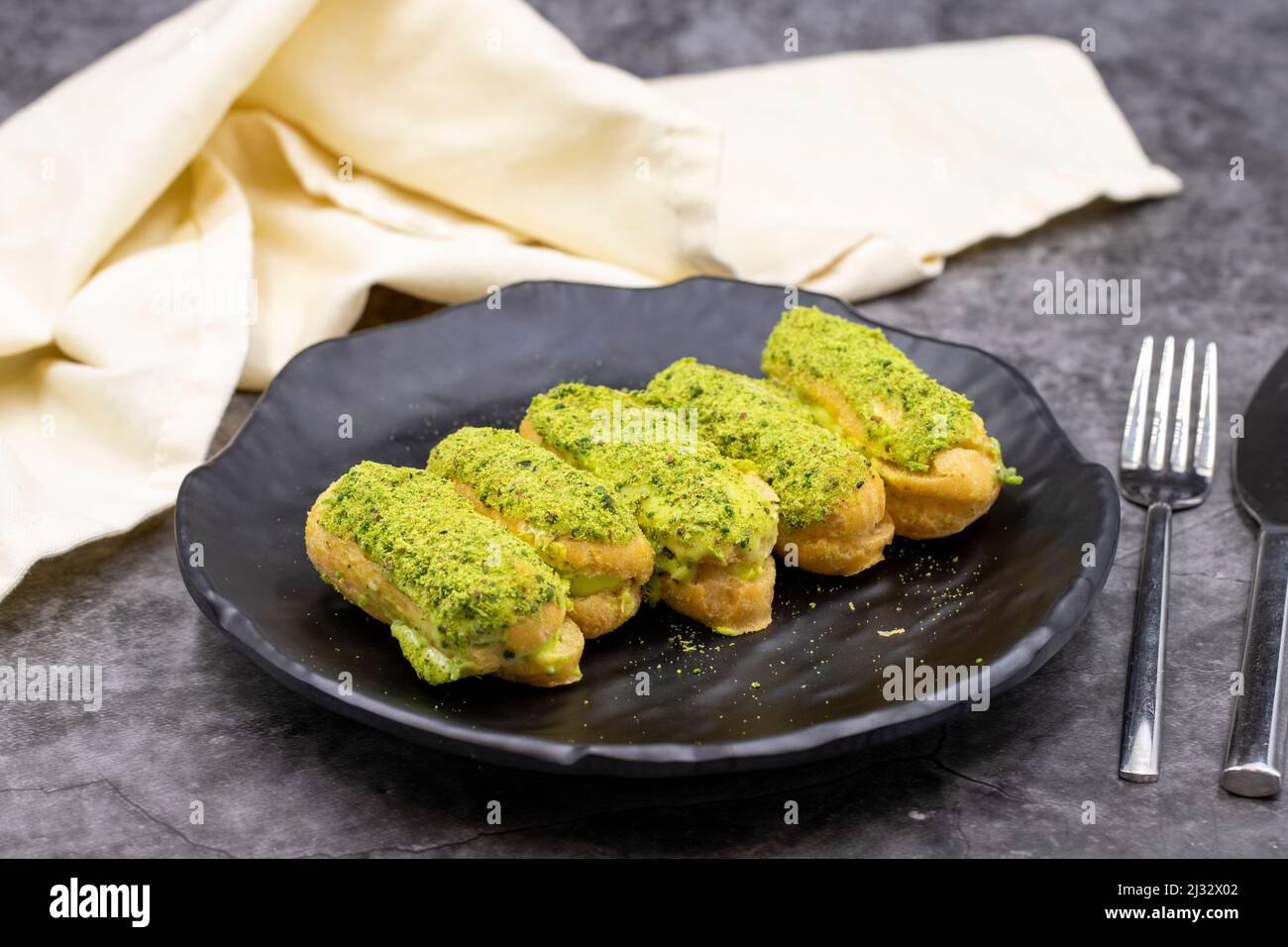 Pistazien-eclair-Kuchen auf dunklem Hintergrund. Köstlichkeiten der Weltküche. Nahaufnahme Stockfoto