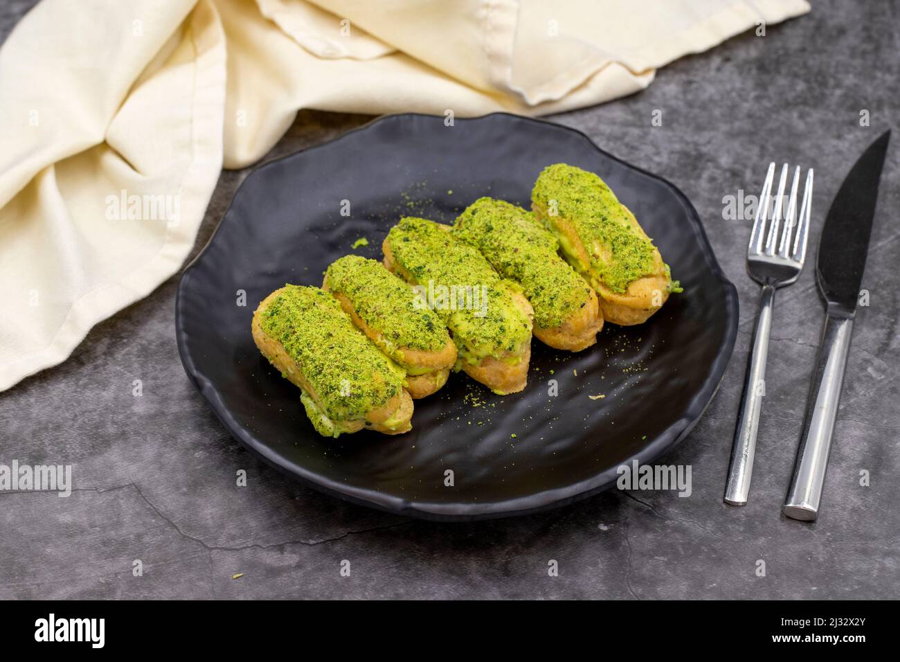 Pistazien-eclair-Kuchen auf dunklem Hintergrund. Köstlichkeiten der Weltküche. Nahaufnahme Stockfoto