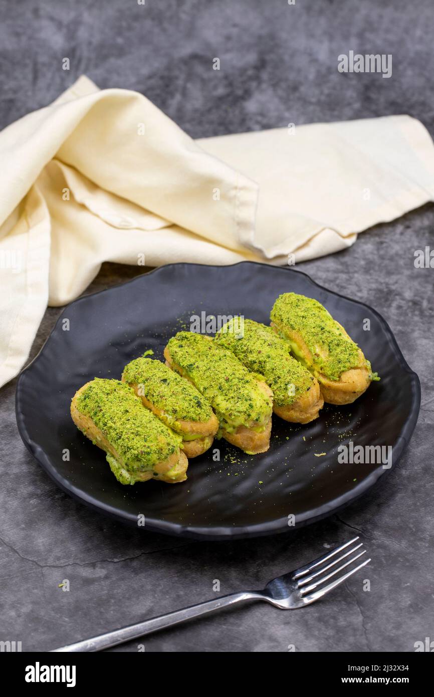 Pistazien-eclair-Kuchen auf dunklem Hintergrund. Köstlichkeiten der Weltküche. Nahaufnahme Stockfoto