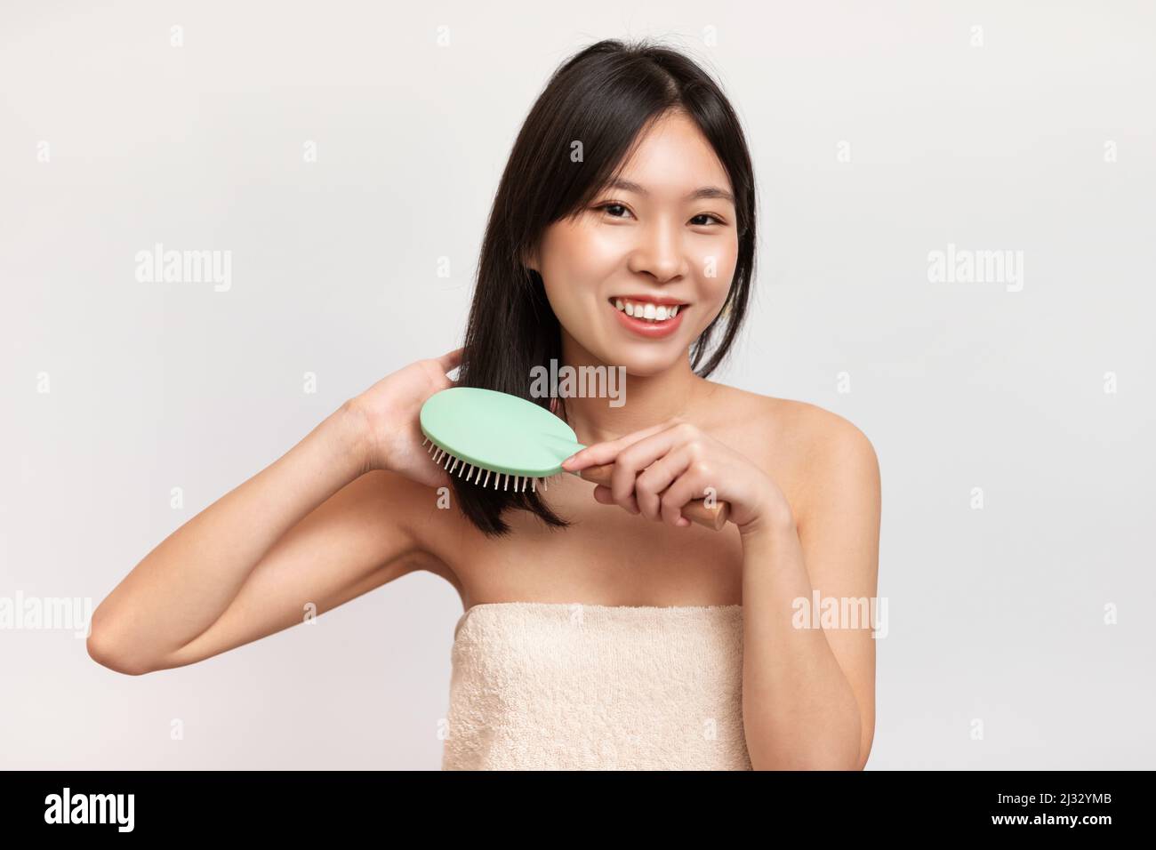 Porträt einer fröhlichen asiatischen Frau, die sich die Haare putzt Stockfoto