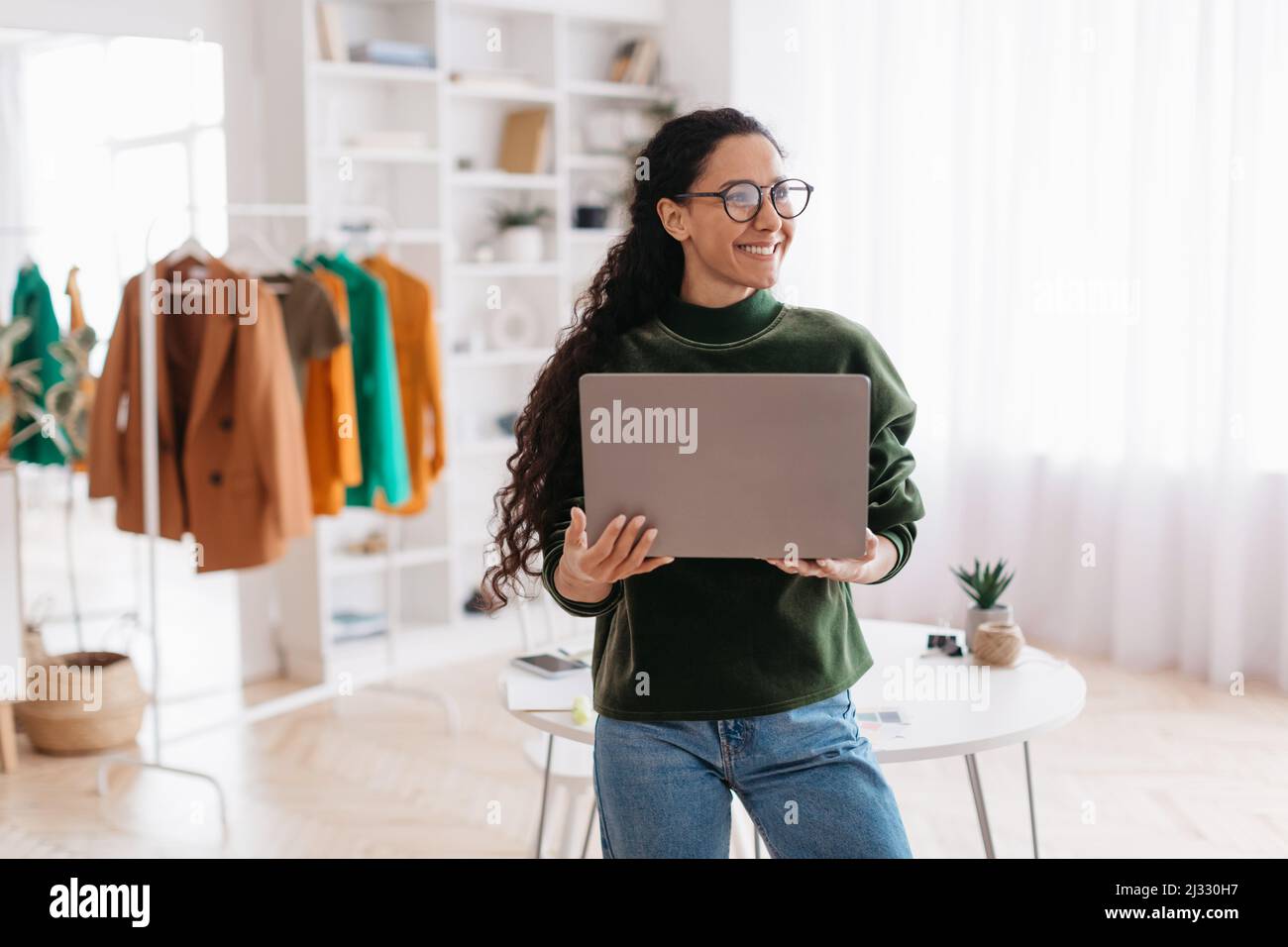 Fröhliche Weibliche Kleidung Designer Holding Laptop Arbeitet Online Im Studio Stockfoto