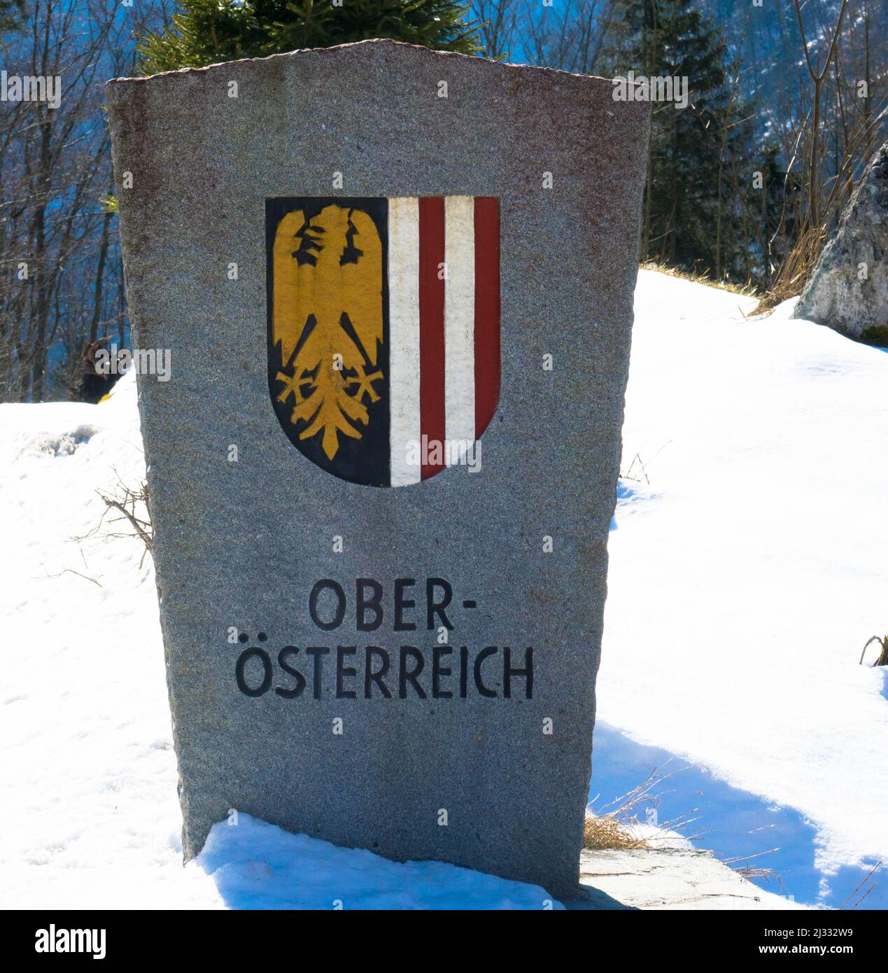 Steinerner Grenzposten von Oberösterreich mit seinem Wappen in Winterlandschaft mit Schnee. Stockfoto