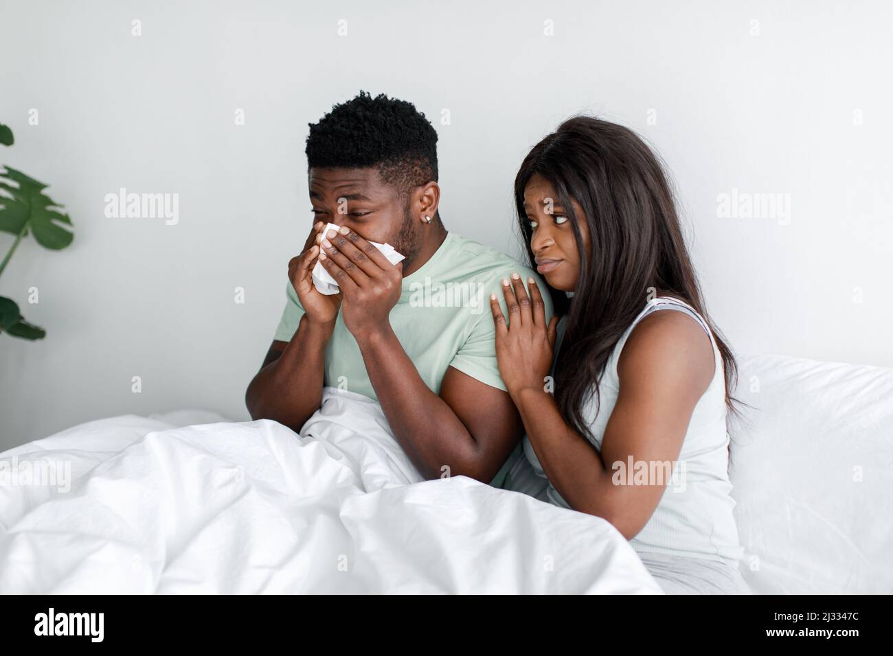 Traurige tausendjährige afroamerikanische Frau Mitleid Ehemann, krank Kerl bläst Nase in Serviette im Bett im weißen Schlafzimmer Stockfoto