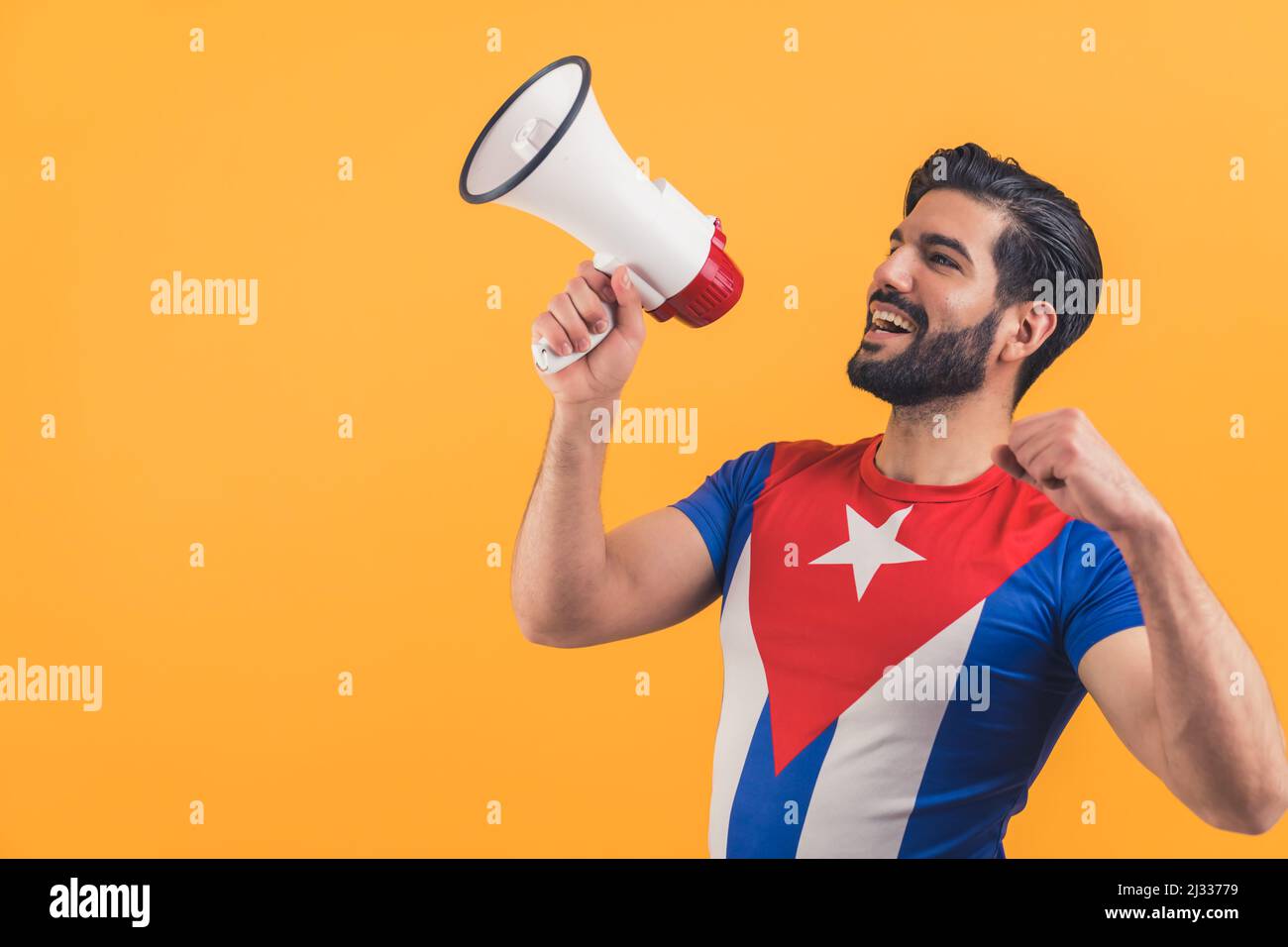Lateinischer bärtiger Mann in kubanischem T-Shirt, der vor orangenen Studiohintergründen zu einem Megaphon schreit. Hochwertige Fotos Stockfoto