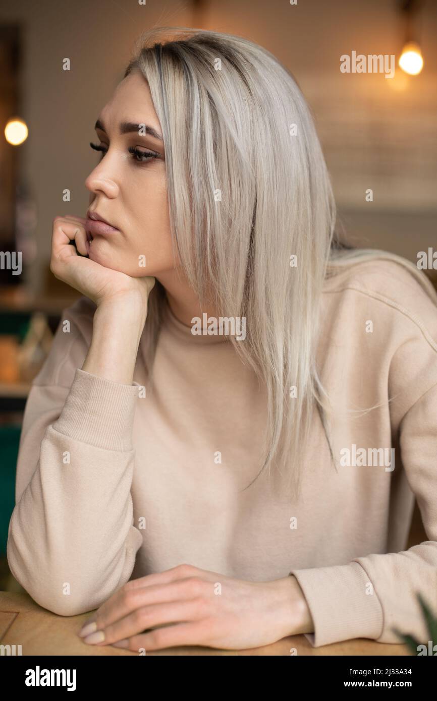 Porträt einer jungen, wunderschönen, nachdenklichen Frau mit langen Haaren und Make-up-Ruhepuls am Kinn, die in Gedanken gestürzt ist. Stockfoto