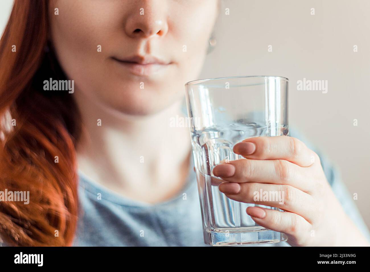 Frau hält ein Glas sauberes Wasser in den Händen. Porträt einer jungen lächelnden rothaarigen Frau. Weltwassertag. Gesundheitskonzept. Stockfoto