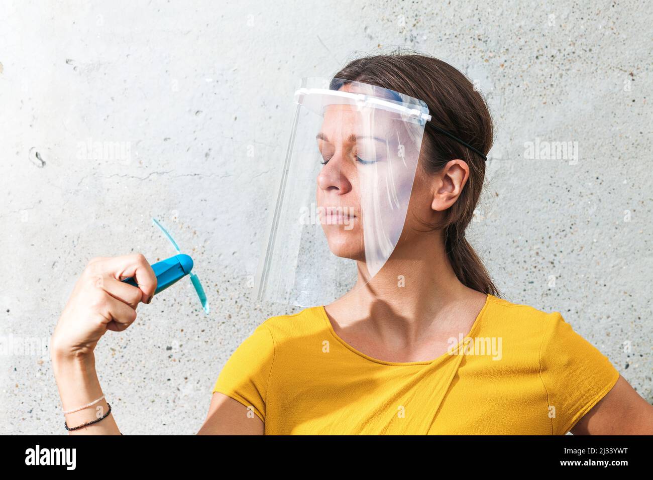 Junge Frau kühlt sich mit einem Handventilator ab, während sie ein Schutzvisier trägt Stockfoto