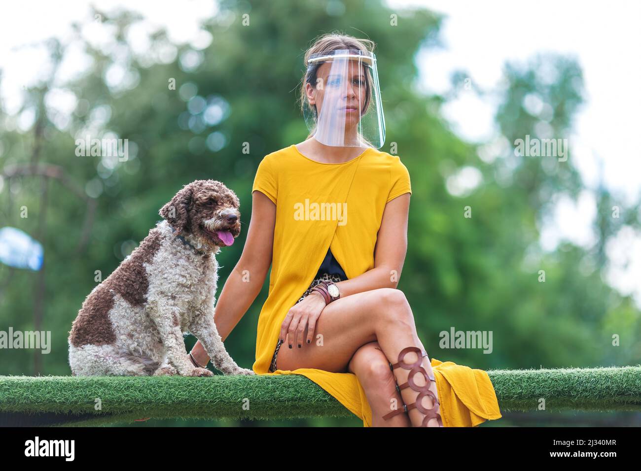 Junge Frau mit Gesichtsvisier sitzt draußen mit ihrem Hund Stockfoto