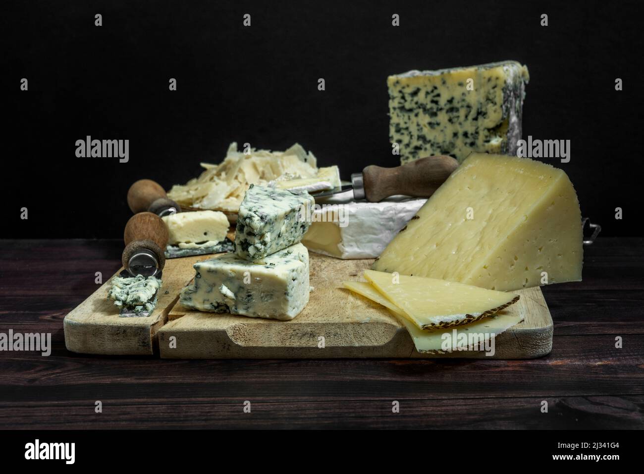 Stillleben mit Schafskäse von Manchego, italienischen Parmesan-Käseflocken und französischem Blauschimmelkäse mit Messern und Knoblauch auf einem Holzbrett Stockfoto