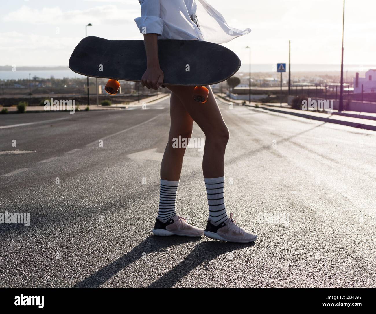 Unbekanntes Skatermädchen, das auf der Straße steht, Skateboard hält, Shorts und gestreifte Socken trägt Stockfoto