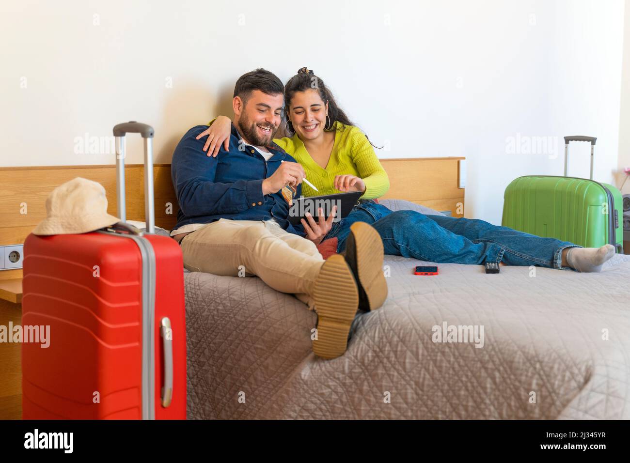 Junges Touristenpaar, das in einem Hotel auf einem Tablet auf dem Bett aufliegt Stockfoto