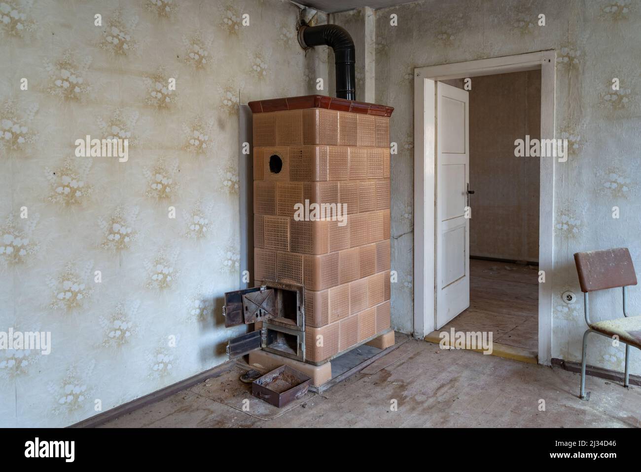 Ein alter Kachelofen in einem Mehrbettzimmer in Ostdeutschland. Verlassene Stelle in einem alten Gebäude. Vintage Innenarchitektur eines verwitterten Hauses. Stockfoto